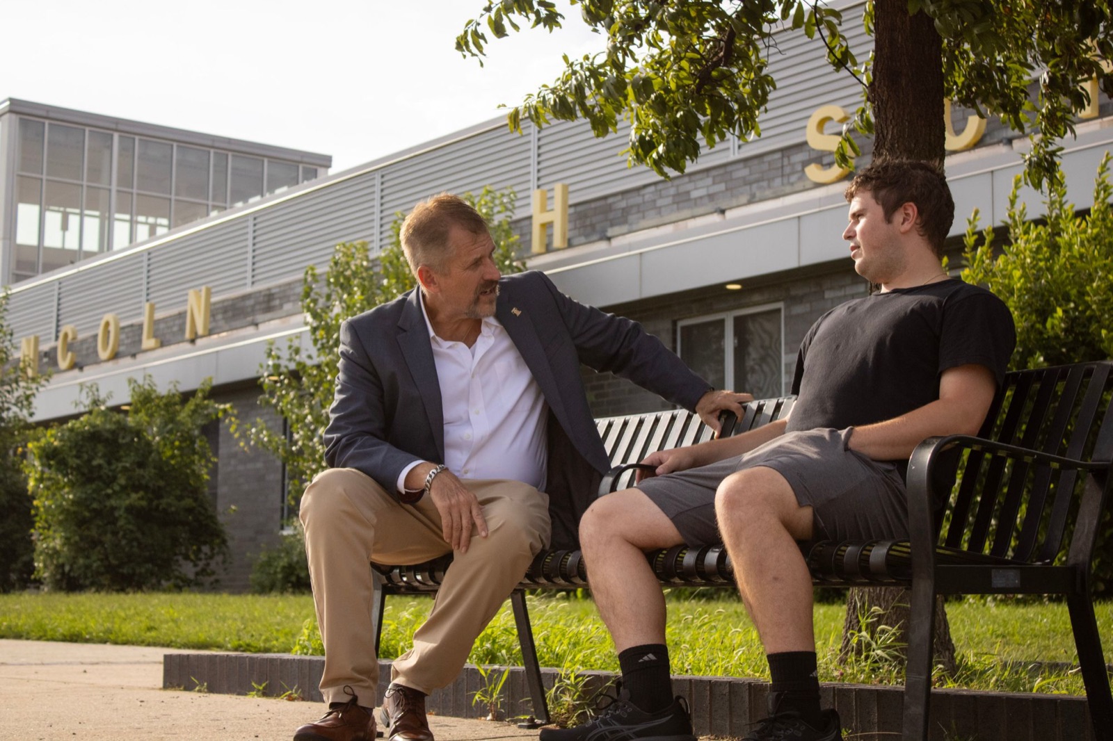 Bill Griffin talking with a young man on a bench outside a Northeast Philadelphia high school